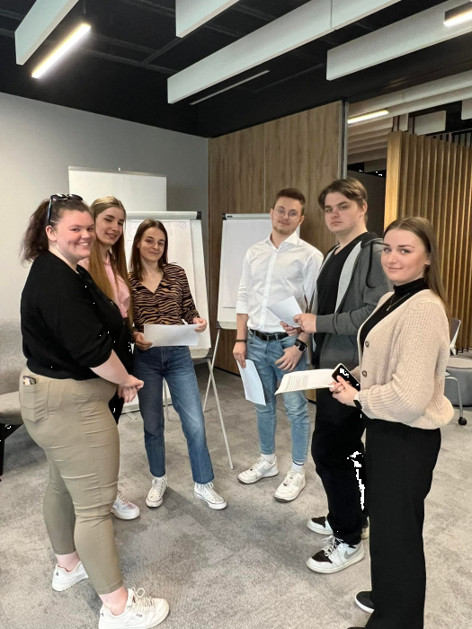 grupa studentów w trakcie pracy w grupach - stoją przy flipchartach z kartkami w rękach