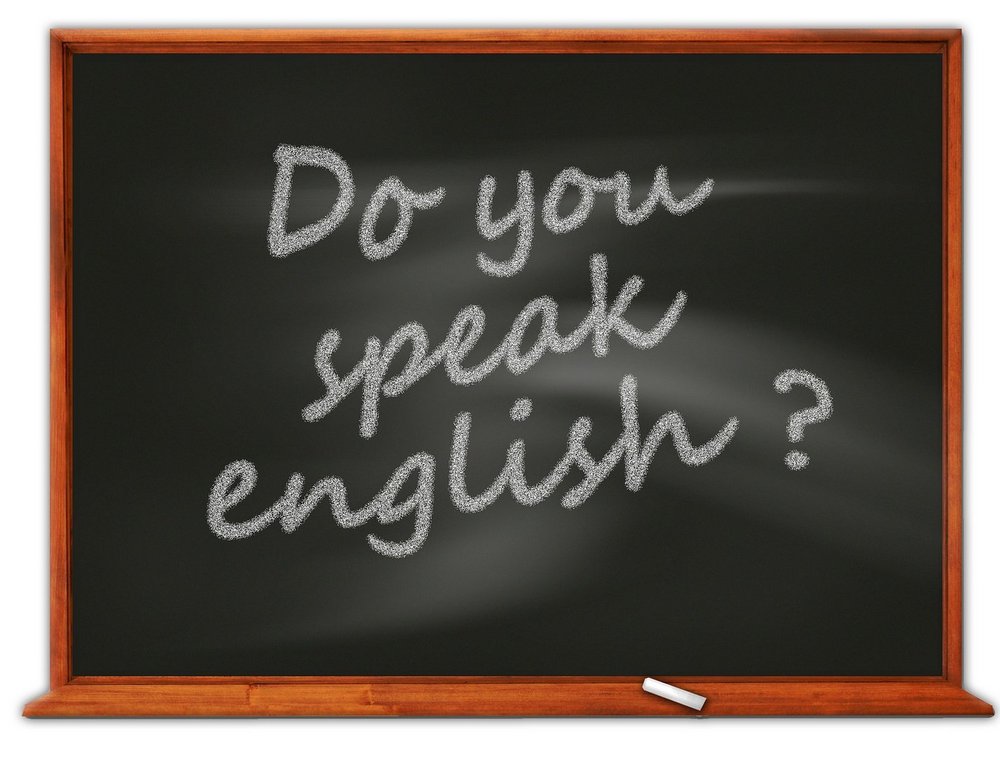 Napis „Do you speak English?” zapisany białą kredą na czarnej tablicy szkolnej z drewnianą ramą.