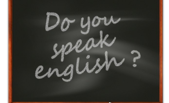 Napis „Do you speak English?” zapisany białą kredą na czarnej tablicy szkolnej z drewnianą ramą.