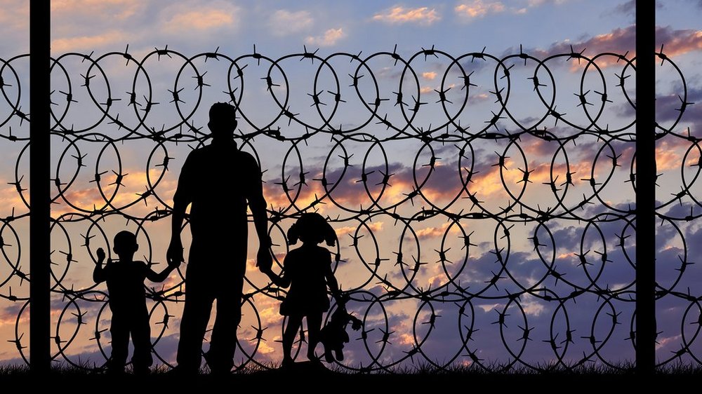 cienie postaci za drutem kolczastym