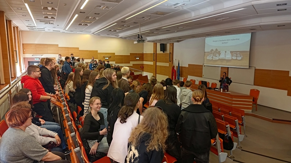 drzwi otwarte 2025 - dr Julita Czernecka prowadzi wykład w auli C101 wypełnionej uczniami i uczennicami szkół średnich, którzy z uśmiechem reagują na prośbę prowadzącej, by wstały osoby mające przynajmniej 3 przyjaciół
