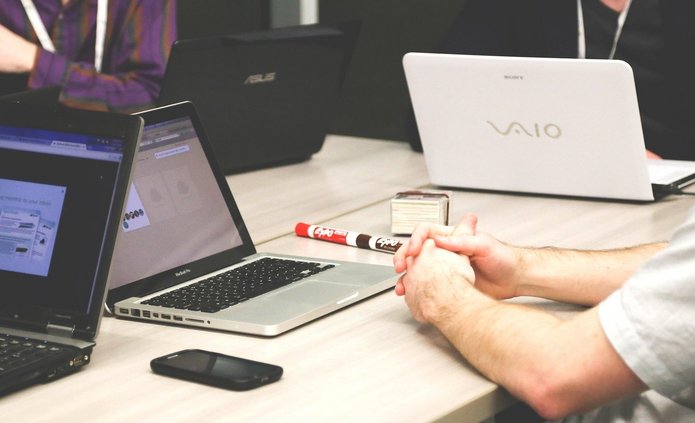 Widok na biurko z otwartymi laptopami, widoczna osoba z boku