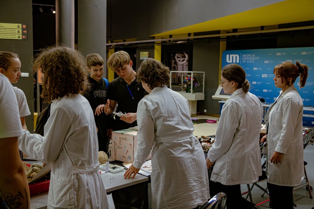 Osoby w białych fartuchach stojące przy stole