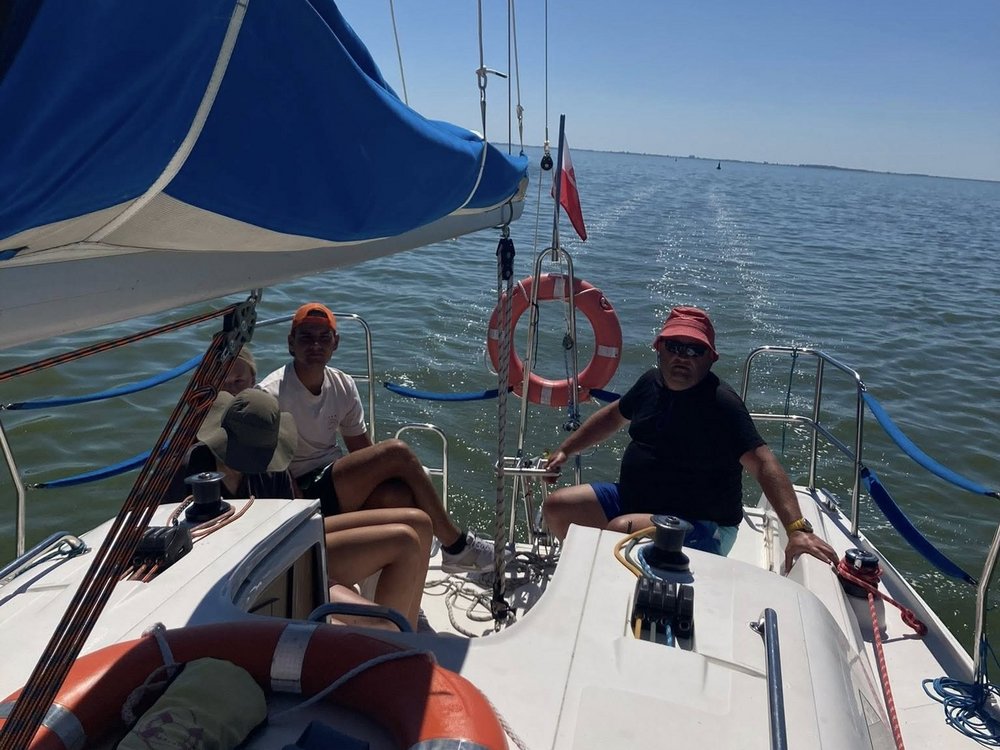 Zdjęcie z jachtu w trakcie rejsu. Widać błękitne niebo i dwóch trenerów, jeden z nich trzyma ster