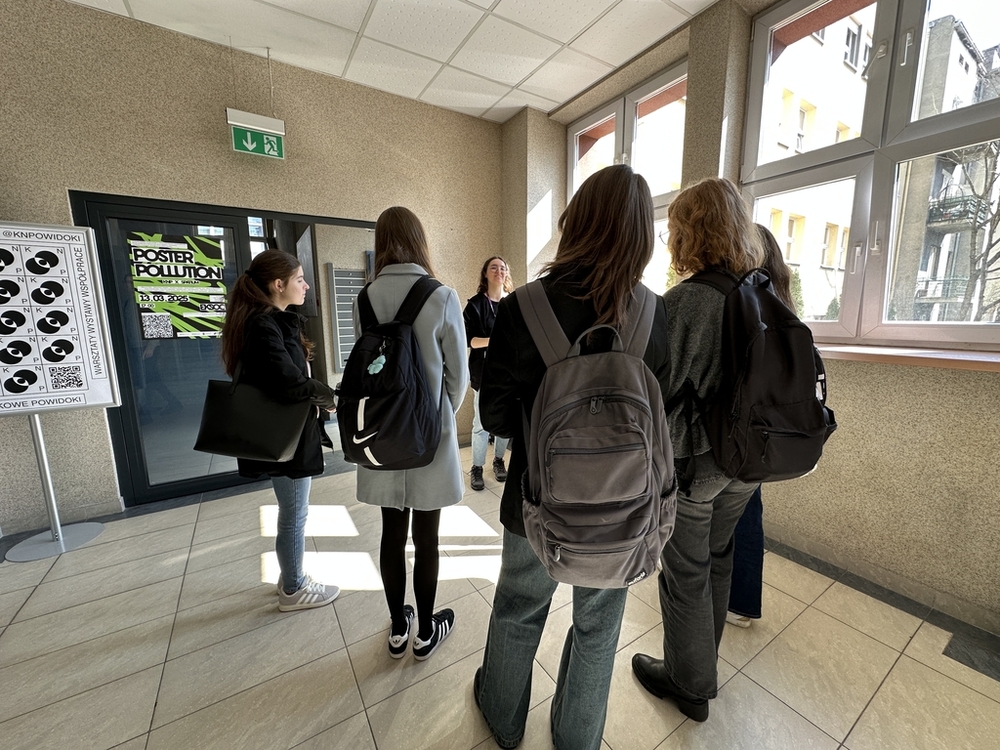 drzwi otwarte 2025 - studentka EkSocu oprowadza po Wydziale 5-osobową grupkę uczniów i uczennic ze szkoł średnich. Zatrzymali się przy wystawie plakatów Poster Pollution, goście słuchają informacji o tej wystawie.