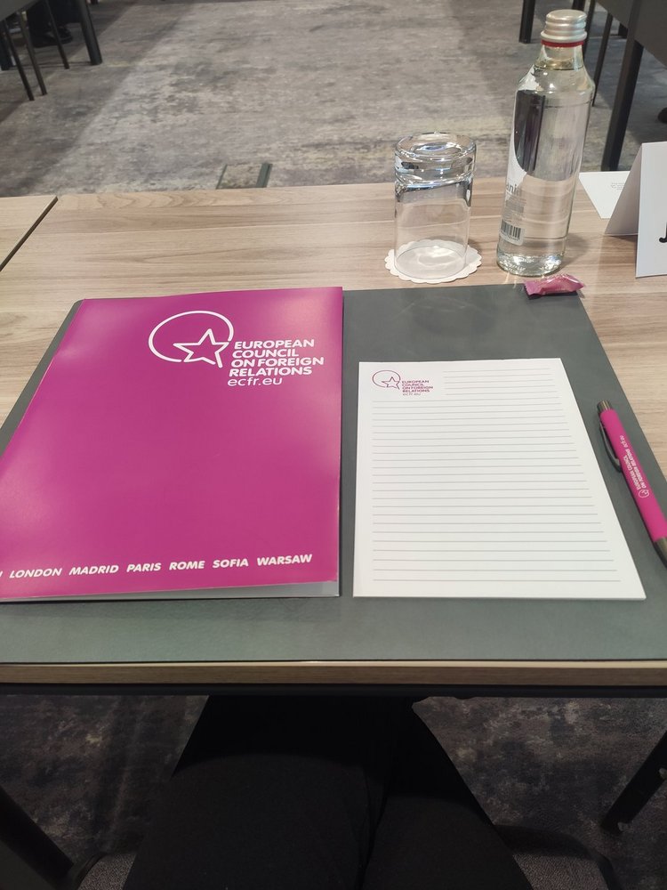 Stolik z teczką z napisem "European Council on Foreign Relations", notatnikiem oraz szklanką i butelką wody 