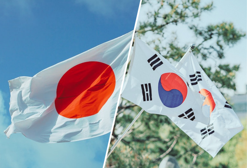 Po lewej stronie biała flaga z czerwonym kołem (flaga Japonii) na tle błękitnego nieba, po prawej stronie dwie białe flagi z czerwono-niebieskim kołem (symbolem taijitu) oraz czterema trygramami (flagi Korei Południowej) powiewające na wietrze na tle zielonych liści drzew i błękitnego nieba